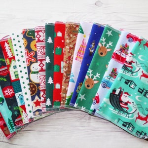 May include: A set of 16 Christmas-themed fabric squares with various patterns, including reindeer, Santa Claus, snowflakes, and gingerbread men. The squares are arranged in a fan shape on a white wooden surface.