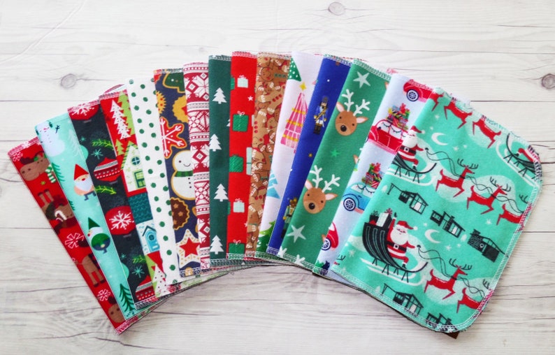May include: A set of 16 Christmas-themed fabric squares with various patterns, including reindeer, Santa Claus, snowflakes, and gingerbread men. The squares are arranged in a fan shape on a white wooden surface.