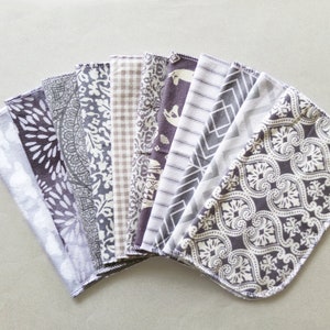 May include: A set of 12 grey and white patterned fabric squares. The squares are arranged in a fan shape and have a variety of different patterns, including geometric, floral, and abstract designs.