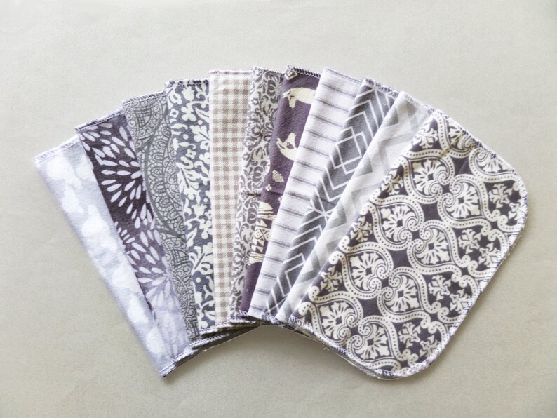 May include: A set of 12 grey and white patterned fabric squares. The squares are arranged in a fan shape and have a variety of different patterns, including geometric, floral, and abstract designs.
