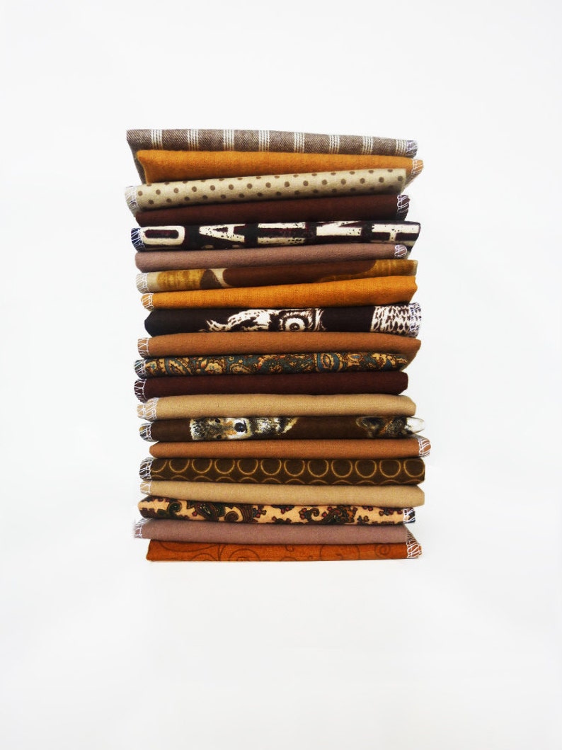 May include: A tall stack of folded fabric in various shades of brown, tan, and orange. The fabrics display a variety of patterns, including polka dots, stripes, and floral designs. The edges of the fabrics are neatly finished.
