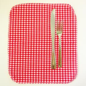 May include: A red and white checkered placemat with a silver knife and fork on top.
