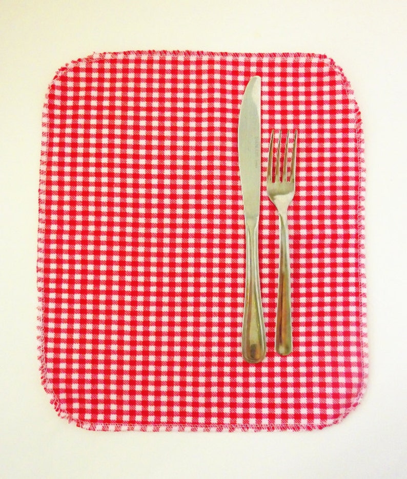 May include: A red and white checkered placemat with a silver knife and fork on top.