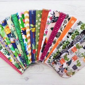 A fan of brightly colored unpaper towels.   Each pattern is different featuring a variety of houseplant, cacti, floral, fruit and retro patterns. Retro patterns include gingham, vine, leaf, daisy.