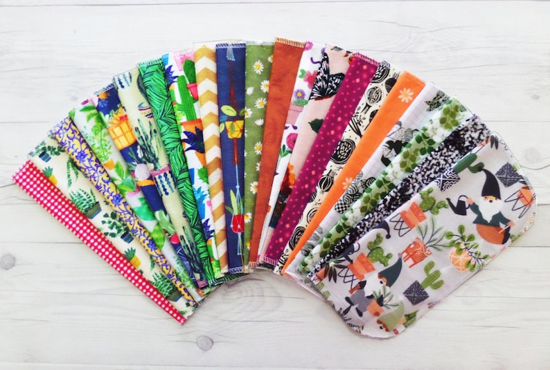 A fan of brightly colored unpaper towels.   Each pattern is different featuring a variety of houseplant, cacti, floral, fruit and retro patterns. Retro patterns include gingham, vine, leaf, daisy.