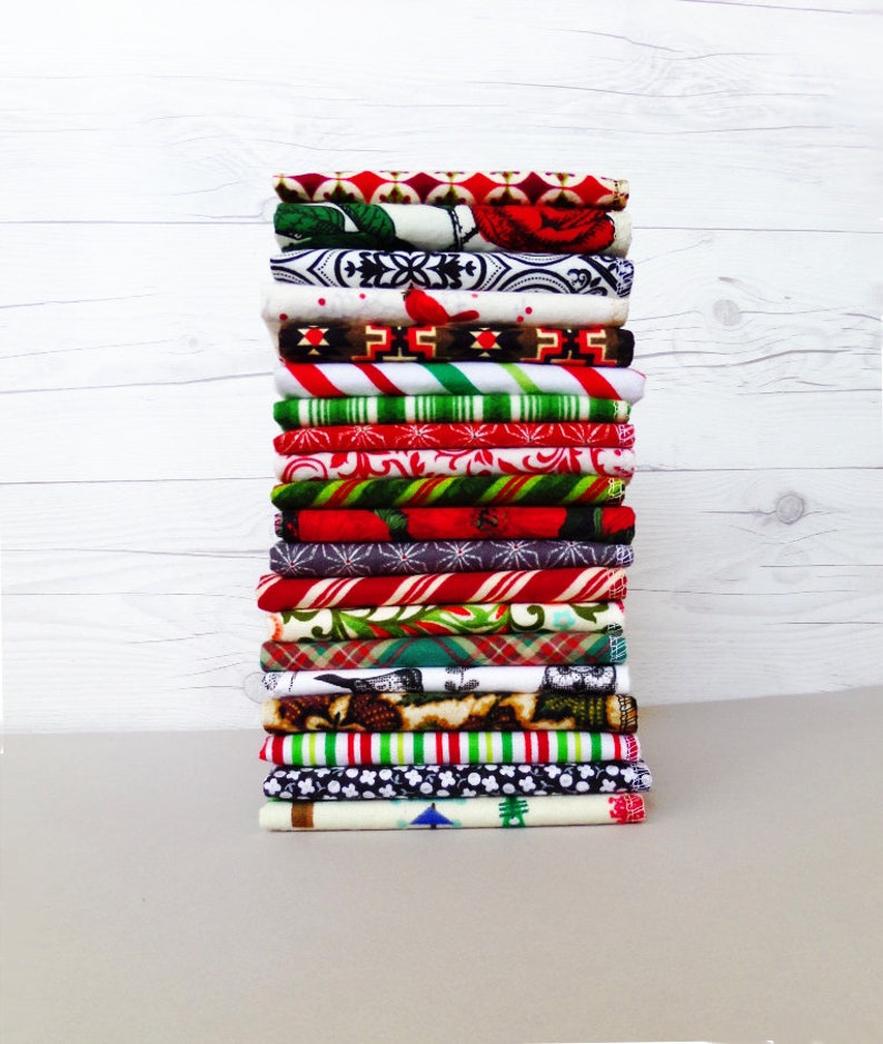 May include: A stack of 18 fabric squares with various Christmas-themed patterns, including red and white candy canes, snowflakes, and plaid.