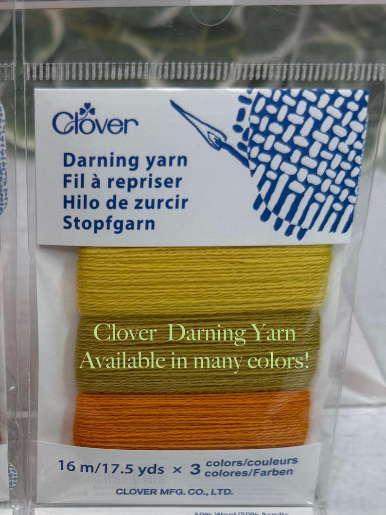 Op de afbeelding: Een verpakking Clover stopgaren in tinten geel en oranje. Het pakket bevat drie kleuren garen, elk 16 meter lang. De verpakking heeft de tekst "Clover Darning Yarn Available in many colors!"