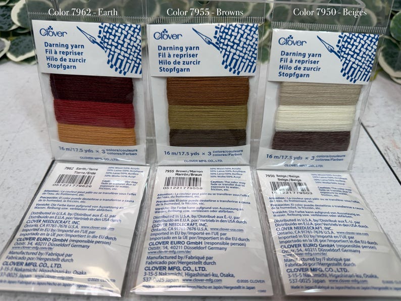 Op de afbeelding: Drie verpakkingen Clover stopgaren in de kleuren Aarde, Bruin en Beige. Elke verpakking bevat drie tinten garen, met 16 m per kleur. De verpakking toont het Clover-logo en productinformatie. Het garen is voor stoppen en repareren.