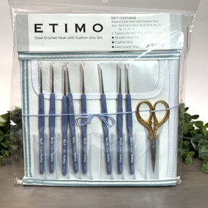 May include: A set of 10 steel crochet hooks with cushion grips, sizes 0-14, in a white case with blue trim. The set also includes two tapestry needles and a pair of gold scissors. The case has the text "ETIMO Steel Crochet Hook with Cushion Grip Set" printed on the front.