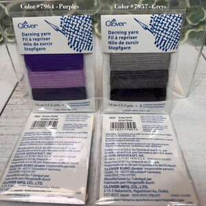Op de afbeelding: Twee verpakkingen Clover stopgaren in doorzichtig plastic. E&eacute;n verpakking is gelabeld "Color #7964 - Purples" en bevat paars garen. De andere is gelabeld "Color #7957 - Greys" en bevat grijs garen. Elke verpakking bevat 16 m garen.