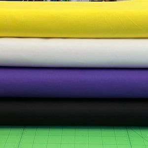 May include: Four rolls of fabric stacked on top of each other. The top roll is yellow, the second roll is white, the third roll is purple, and the bottom roll is black.