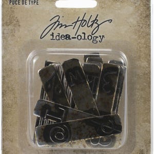 May include: A pack of dark grey metal type chips, featuring numbers and letters. The rectangular chips have a distressed finish. The packaging includes the text "TYPE CHIPS" and "42 PIECES/42 PIÈCES". The brand name "Jim Holtz idea-ology" is also visible.