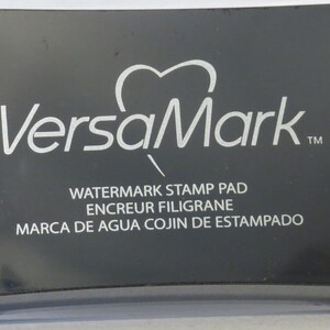 May include: Black VersaMark watermark stamp pad with the text "Watermark Stamp Pad", "Encreur Filigrane", and "Marca de Agua Cojin de Estampado".