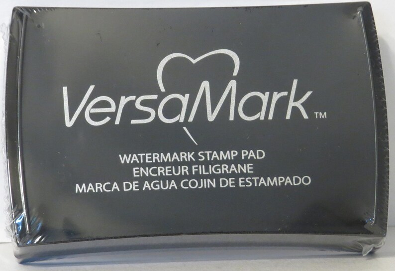 May include: Black VersaMark watermark stamp pad with the text "Watermark Stamp Pad", "Encreur Filigrane", and "Marca de Agua Cojin de Estampado".