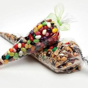 May include: Two clear plastic cone-shaped bags filled with food items. One bag contains a variety of colourful jelly beans and is tied with a light green ribbon. The second bag contains a mixture of nuts, seeds, and dried fruit, tied with black and white twine.