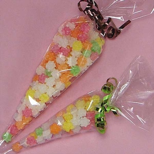 May include: Two clear cone-shaped plastic bags filled with small, star-shaped sugar sweets in white, yellow, orange, pink, and green. The larger bag is tied with a brown curling ribbon, and the smaller bag is tied with a green curling ribbon.