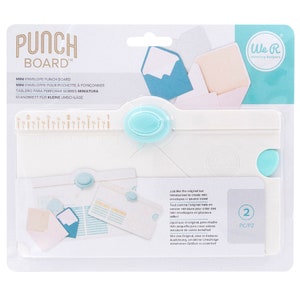 May include: White plastic punch board with a blue handle and ruler for creating mini envelopes. The packaging includes the text "Punch Board" and "We R Memory Keepers".