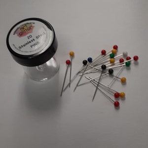 May include: A clear plastic jar with a black lid containing 20 stainless steel pins. The pins have colorful round heads in red, yellow, green, blue, and black. The jar is next to a scattering of the pins.