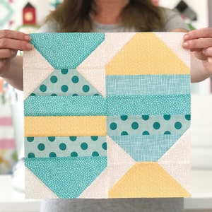 May include: A quilt block with a geometric pattern in shades of teal, yellow, and white. The block is made up of squares, triangles, and rectangles, and features a variety of patterns, including polka dots, stripes, and a small-scale geometric print.