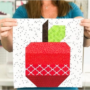 Puede incluir: Un cuadrado de tela blanco con lunares negros presenta un diseño de manzana de patchwork rojo y verde. La manzana está hecha de diferentes telas con patrones geométricos. El texto "The Sewing Loft" es visible en la esquina inferior derecha.