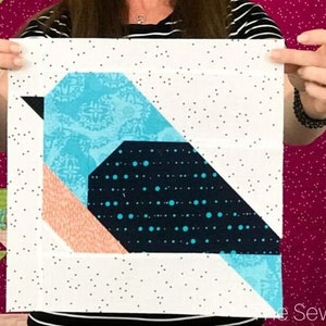 Könnte beinhalten: Ein weißer Stoffquadrat mit einem geometrischen Design, das eine blaue, schwarze und pfirsichfarbene Vogelform zeigt. Der Stoff hat einen weißen Hintergrund mit kleinen schwarzen Punkten.