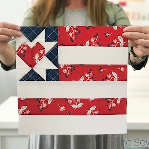 Op de afbeelding: Een handgemaakt quiltblok met een patriottisch ontwerp. Het blok bevat rode, witte en blauwe stoffen, met een hart- en stermotief in de linkerbovenhoek. De rode stof heeft een bloemenpatroon. Het logo The Sewing Loft is zichtbaar.