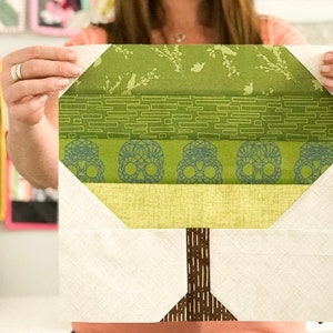 May include: A green and white patchwork quilt block featuring a stylized tree design. The tree has a brown trunk and green leaves with a white background. The leaves are made up of different patterns, including a brick pattern and a skull pattern.