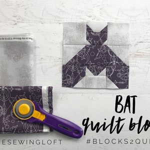 May include: A purple and white fabric quilt block in the shape of a bat. The fabric has a geometric pattern. The text "BAT quilt block #BLOCKS2QUILT" is below the block.