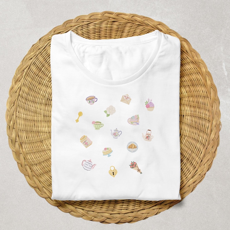 May include: White t-shirt with various embroidered pastel-colored illustrations of teacups, teapots, pastries, and flowers. The shirt is folded on a round, woven wicker surface.