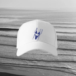 May include: White baseball cap with a blue outline of a bikini. The cap has a curved peak and a structured crown. The background is a grayscale image of the sea.