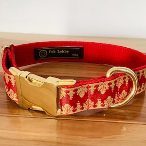 Może przedstawiać: Czerwono-złoty obroża dla psa ze złotą klamrą i złotym kółkiem D. Obroża ma wzór w kolorze złotym i czerwonym. Na obroży widnieje napis "Fab Lobby USA".