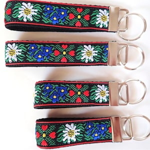 Llavero EDELWEISS. Llavero de jacquard rojo, blanco, azul y verde sobre cincha negra. Herrajes de níquel plateado. Pulsera. 1" de ancho, tamaño a elegir