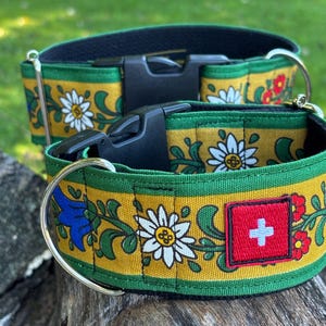 Puede incluir: Dos collares para perro con fondo amarillo mostaza y un patrón floral de margaritas blancas, campanillas azules y flores rojas. Cada collar tiene una hebilla de plástico negro, una anilla en D de metal y un parche cuadrado con la bandera suiza.