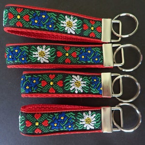 Llavero EDELWEISS. Llavero jacquard rojo, blanco, azul, verde sobre negro. Correa roja. Herrajes de níquel plateado. Pulsera. 2,5 cm de ancho. Variedad de tamaños y estilos.