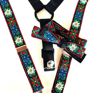 Puede incluir: Tirantes negros con un estampado floral decorativo en rojo, verde, azul y blanco. Los tirantes tienen clips plateados y un diseño negro con anillo y correa.
