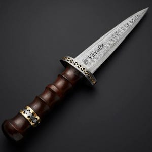 Puede incluir: Una daga de acero Damasco con mango de madera oscura y detalles dorados. La hoja está grabada con el texto "Yjcraft".