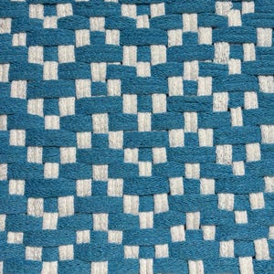 Op de afbeelding: Een geweven textielstof met een herhalend geometrisch patroon van blauwgroene en gebroken witte draden. Het materiaal vertoont een dichte, verweven constructie waarbij de horizontale blauwgroene strengen afwisselen met verticale witte strengen.