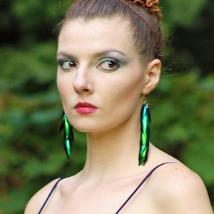 Puede incluir: Una mujer con el pelo castaño recogido en un moño lleva un vestido azul oscuro sin mangas con un escote pronunciado. Lleva pendientes largos de color verde y azul.