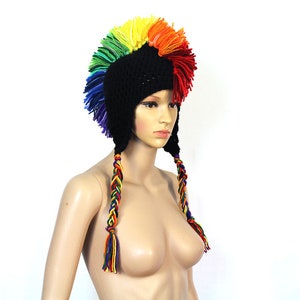 Peut inclure: Un bonnet en crochet noir avec une crête mohawk arc-en-ciel et de longues tresses arc-en-ciel. Le bonnet est porté sur une tête de mannequin.