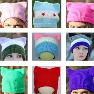 May include: A collection of 15 colorful knit hats with cat ears. The hats are in various colors, including rainbow, pink, blue, green, red, purple, and gray. Some hats feature stripes or other patterns.