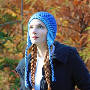 May include: A woman with long, braided red hair wears a blue knitted hat with ear flaps and a dark blue coat.