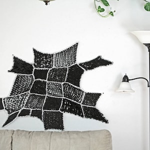Puede incluir: Un tapiz de pared de crochet blanco y negro con un diseño geométrico. El tapiz está hecho de hilo y tiene una superficie texturizada.