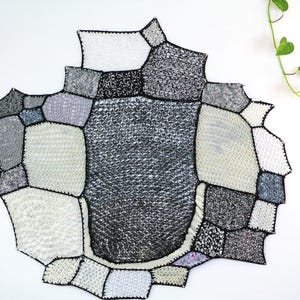 Puede incluir: Un tapiz de pared de crochet blanco y negro con un patrón geométrico. El tapiz está hecho de cuadrados y círculos de diferentes tamaños.