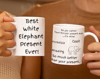 May include: Two white ceramic mugs with black text. One mug reads "Best White Elephant Present Ever!". The other mug has an elephant graphic and text that says "No you cannot have the best present ever...it's mine!" and "So much better than your present."