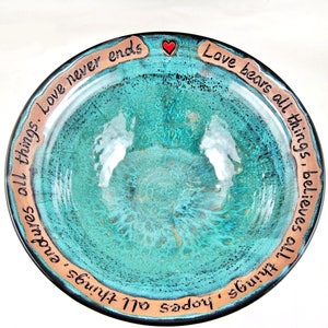 May include: A turquoise ceramic bowl with a brown rim and a red heart. The rim is inscribed with the text "Love bears all things, believes all things, endures all things. Love never ends".