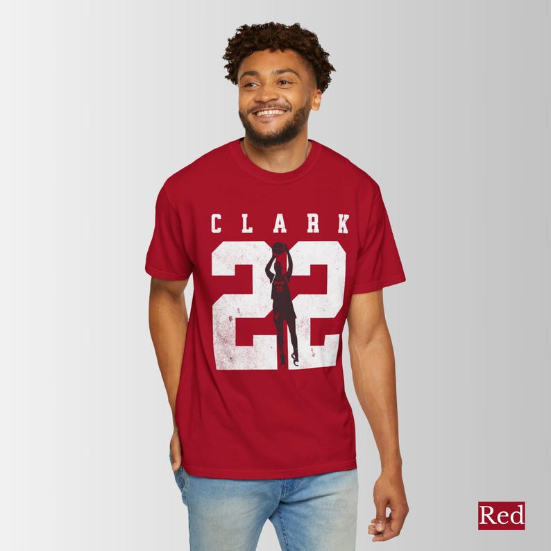 May include: Red t-shirt with the name "CLARK" and the number "22" in white, featuring a silhouette of a basketball player. The shirt is worn by a person.
