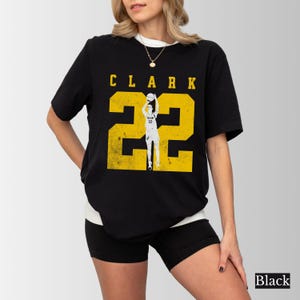 May include: Black t-shirt with a yellow graphic that says "CLARK 22" with a basketball player silhouette. The shirt is worn with black shorts and a white undershirt. The word "Black" is in the bottom right corner.