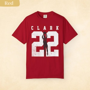 May include: Red t-shirt with the name "CLARK" above the number "22" in white, with a silhouette of a basketball player in the center. The shirt is a solid red color.