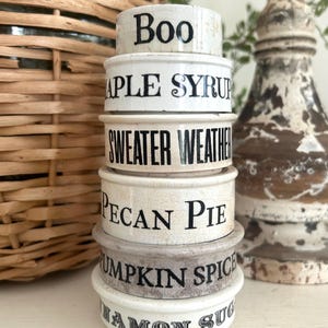 May include: A stack of six white ceramic ramekins with a crackled glaze finish and black text. The text on the ramekins reads Boo, Maple Syrup, Sweater Weather, Pecan Pie, Pumpkin Spice, and Cinnamon Sugar in a stacked vertical arrangement.