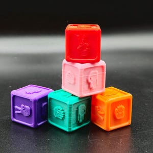 May include: A set of six colourful, square-shaped blocks with different symbols on each side. The blocks are stacked in a pyramid shape, with the top block being red, the second block being pink, the third block being purple, the fourth block being green, and the fifth block being orange.